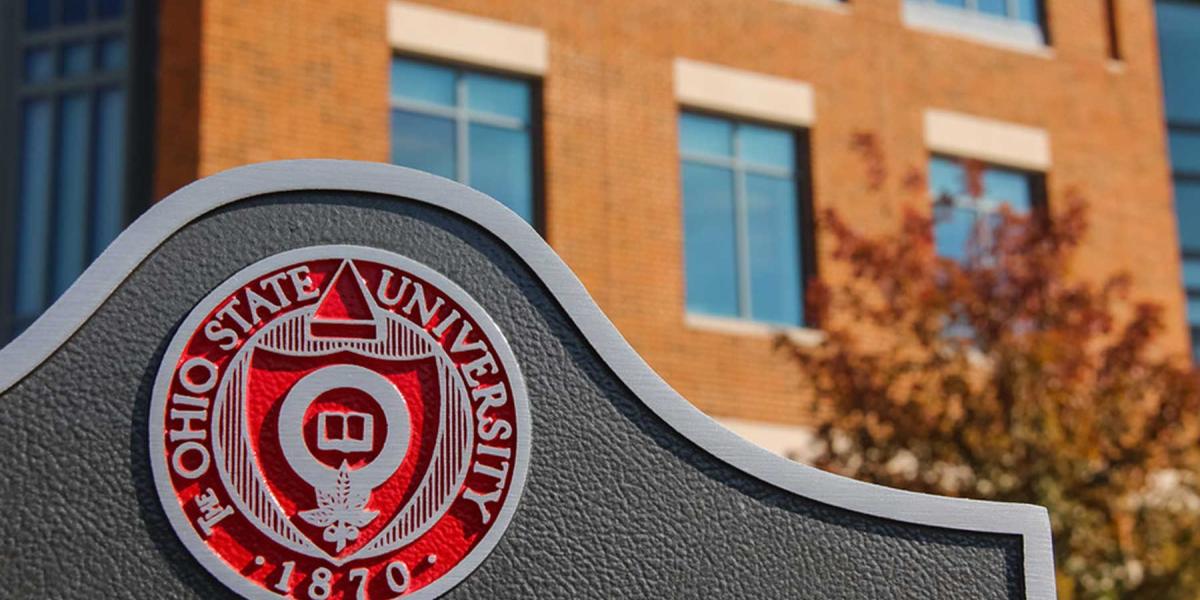 Picture of the seal of The Ohio State University on a sign with a brick building in the background.